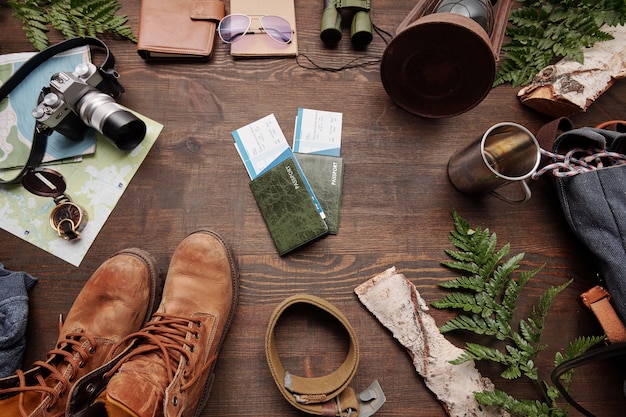 A macro shot of various essential ecotourism gear laid out on a wooden surface, including a hiking boot, a water bottle, sunscreen, insect repellent, and a map.