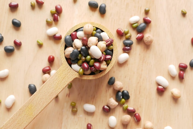 A close-up shot focusing on various types of beans (black, carioca, white, red) and other legumes (lentils, chickpeas) in separate bowls, arranged on a rustic wooden table. The lighting should highlight the textures and colors of the different grains.