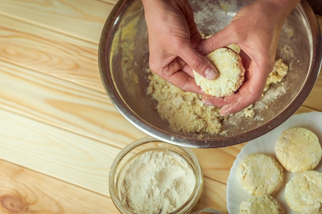 A close-up shot of a hand mixing ingredients for pão de queijo in a large bowl. The bowl contains a mixture of polvilho, eggs, grated queijo minas, and melted butter. The hand is holding a wooden spoon and carefully incorporating the ingredients. The background is a clean kitchen counter with various utensils and ingredients neatly arranged.