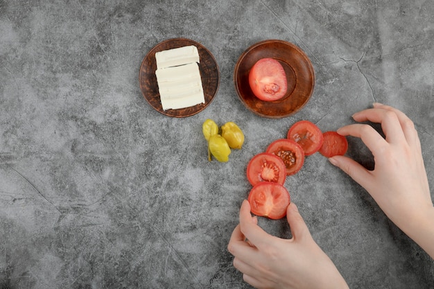 A top-down view of a chef carefully adding diced tomatoes and onions to a clay pot filled with seasoned fish fillets during the preparation of Moqueca Capixaba in a professional kitchen setting. There's a focus on the vibrant colors and textures of the fresh ingredients.