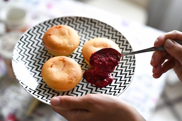 A close up of vegan pão de queijo being served. The bread is golden brown and its crust is slightly cracked. A small dish of guava jam sits nearby, ready to be spread.