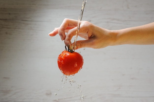 close-up shot of someone's hand carefully washing organic tomatoes in a kitchen sink, highlighting the vibrant red color and natural imperfections of the tomatoes.