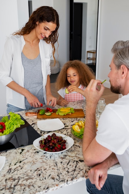 A family, including parents and children, are preparing a healthy organic meal together in their bright and modern kitchen, smiling and engaging with each other.