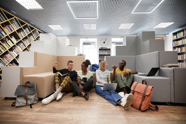 A diverse group of students studying in a modern library, with laptops and books spread across the tables. Some are working individually, while others are collaborating on projects, creating a vibrant and focused atmosphere.