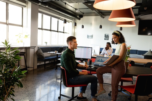 A modern office space in a co-working environment, with people working on laptops and collaborating on projects. The image captures a tech-focused company providing digital services, with elements like monitors displaying code and creative brainstorming sessions. Natural light and contemporary design.