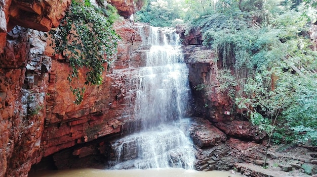 A picturesque scene of the Chapada dos Veadeiros National Park, featuring a cascading waterfall flowing into a clear pool, surrounded by lush green vegetation and unique rock formations. Capture the serene beauty of the natural landscape and the sense of adventure and exploration. Include hikers in the background to showcase the park's appeal for outdoor enthusiasts.