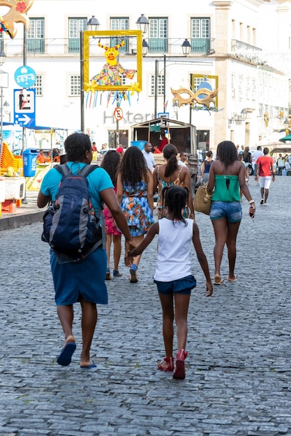 A street scene in Salvador, Bahia, Brazil, showing a mix of locals and tourists. The tourists are discreetly checking maps on their phones, while locals are engaged in everyday activities. The focus is on responsible tourism.