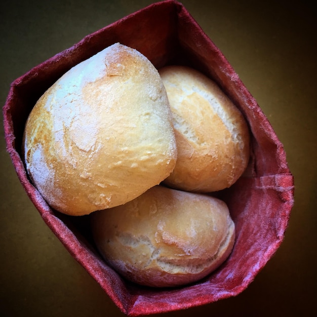 A close-up of a basket filled with golden, freshly baked pão de queijo, displaying their slightly crispy exterior and soft, cheesy interior. The background includes a blurred view of a traditional Minas Gerais kitchen with rustic elements.